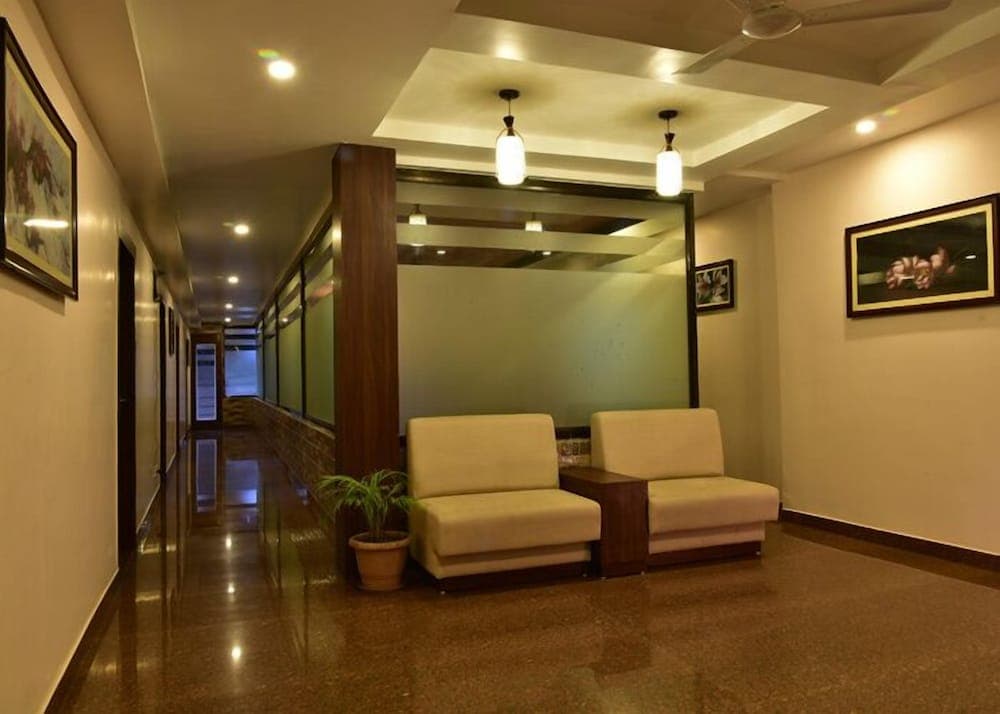 A cozy hotel lobby features soft lighting, comfortable beige armchairs, framed artwork on cream walls, and a polished floor, creating a welcoming atmosphere ideal for travelers seeking relaxation.