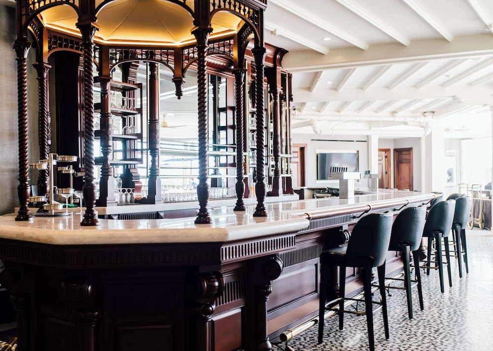 An elegant bar with ornate wooden columns and a polished countertop invites travelers to unwind in a sophisticated lounge setting, perfect for a relaxing drink or social gathering.