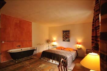 A cozy bedroom with warm lighting, a freestanding bathtub, and vibrant orange accents creates an inviting atmosphere ideal for a relaxing getaway.