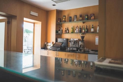 A cozy café interior with wooden shelves stocked with bottles, a sleek espresso machine, and an inviting outdoor view through the doorway, perfect for travelers seeking a relaxing coffee break.