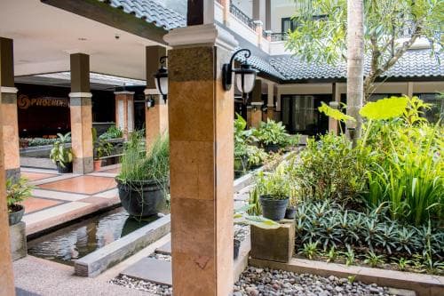 A serene courtyard with lush greenery, stone pathways, and traditional architecture creates an inviting atmosphere ideal for relaxation at a resort or hotel.