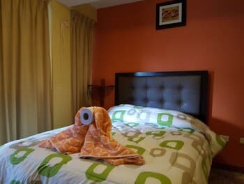 A cozy hotel room with an orange wall, neatly made bed adorned with a playful towel monster, and warm curtains, ideal for travelers seeking comfort and whimsy.