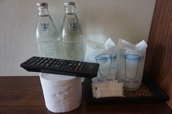 A cozy hotel room bedside table features a tray with neatly arranged toiletries, water bottles, glasses, and a remote control, evoking a sense of comfort and convenience for travelers seeking relaxation.