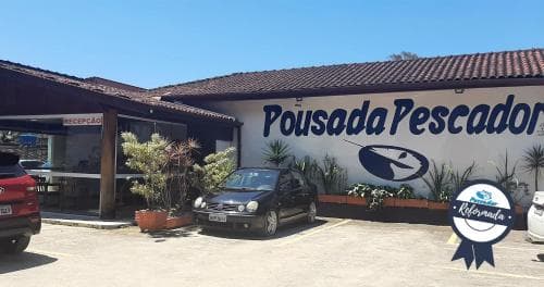 A cozy beachside pousada with a welcoming facade, parked cars, and tropical plants offers travelers a serene retreat in a sunny coastal setting.