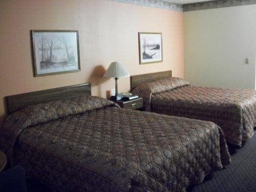 A cozy motel room features two neatly made beds with patterned quilts, framed nature artwork on soft peach walls, and a bedside lamp, ideal for travelers seeking a comfortable and budget-friendly stay.