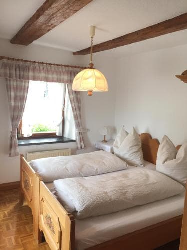 A cozy bedroom with wooden beams, checkered curtains, and neatly arranged beds exudes warmth and comfort, ideal for travelers seeking a peaceful retreat in a rustic lodge.