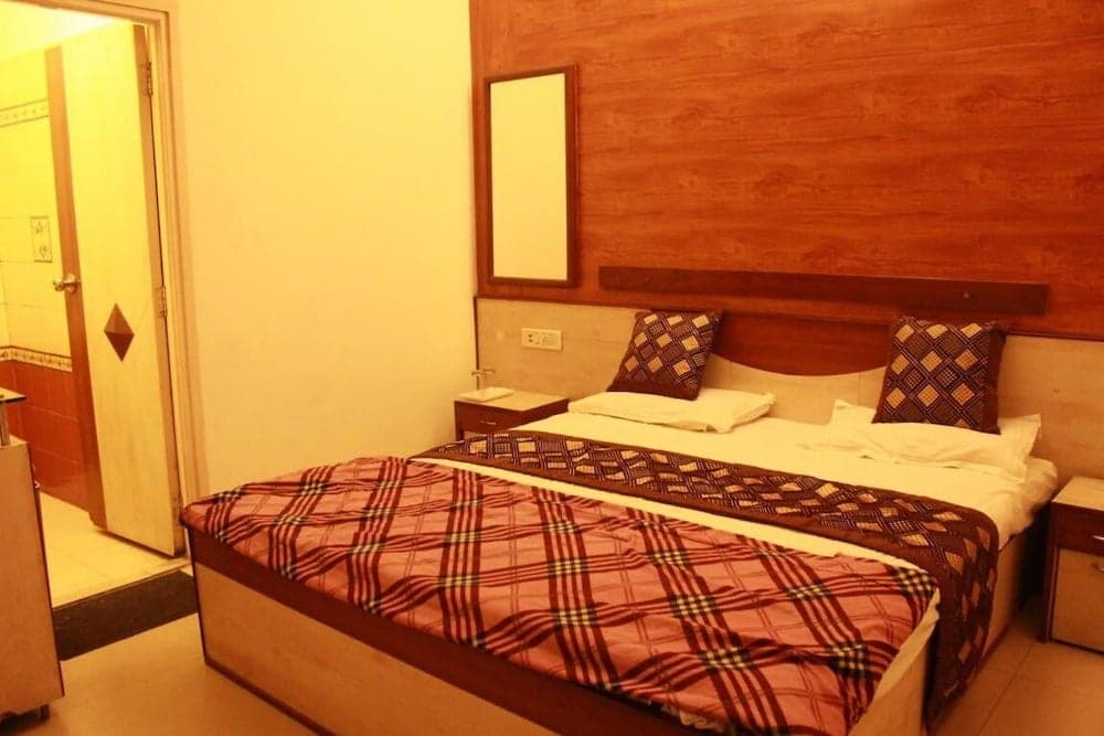 A cozy hotel room features a neatly made bed with patterned bedding, wooden accents, and a warm ambiance, ideal for travelers seeking comfort and relaxation.