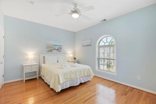 A serene bedroom with light blue walls, hardwood floors, and an arched window offers a cozy retreat, ideal for travelers seeking relaxation in a vacation rental.