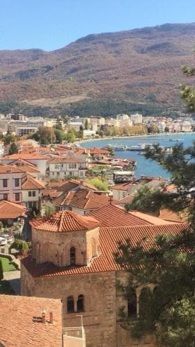 A serene lakeside town with red-roofed buildings and a historic church overlooks calm waters against a backdrop of autumn-hued mountains, ideal for tranquil cultural exploration.