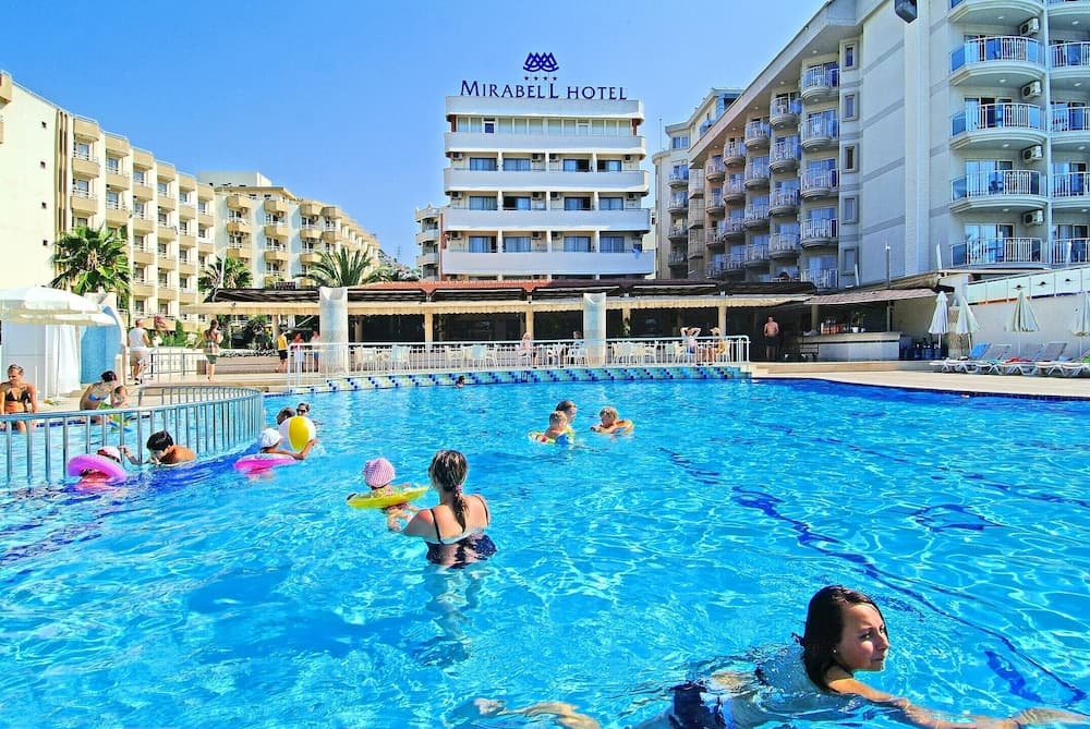 A vibrant pool scene at the Mirabell Hotel features families enjoying colorful floaties under sunny skies, ideal for family vacation imagery.