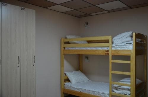 A cozy hostel room features wooden bunk beds with neatly arranged bedding, a wardrobe labeled "505" and "506," and a simple tiled ceiling, ideal for budget travelers seeking comfortable accommodation.