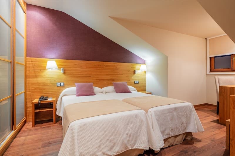 A cozy hotel room in Asturias, Spain, features twin beds with plush bedding, wooden accents, and warm lighting, ideal for travelers seeking comfort and relaxation.