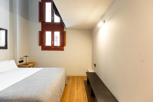 A cozy attic bedroom with wooden floors, slanted ceilings, and rustic window shutters offers a serene retreat for travelers seeking a quaint and charming accommodation experience.