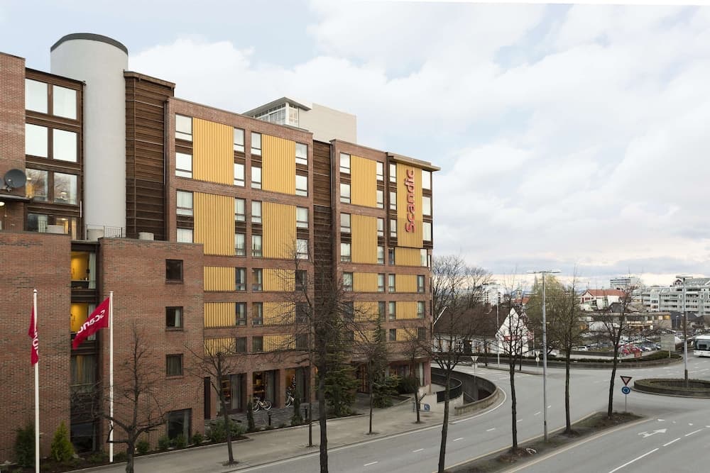 A modern urban hotel with distinctive yellow paneling stands along a quiet street lined with bare trees under a partly cloudy sky, ideal for travelers seeking city accommodations with easy access to local attractions.