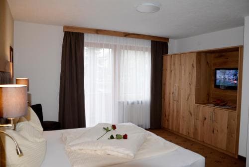 A cozy hotel room features a neatly made bed adorned with roses, wooden furniture, a TV, and soft lighting, creating a warm and inviting atmosphere ideal for relaxation during a getaway.