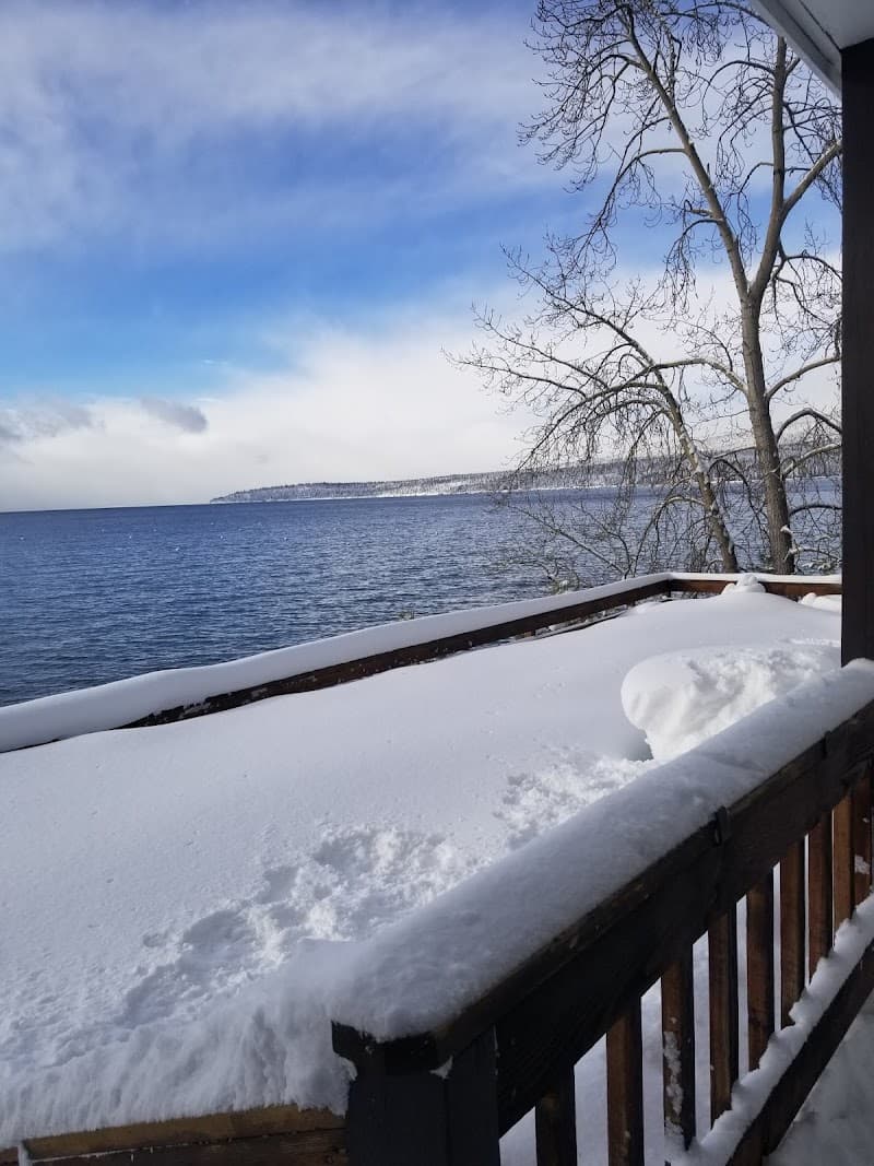 A serene winter scene features a snow-covered deck overlooking a vast lake under a partly cloudy sky, ideal for a tranquil lakeside getaway.