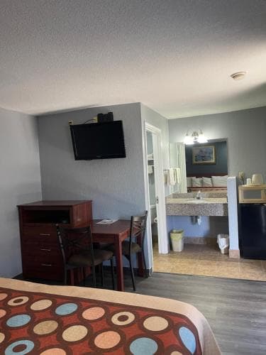 A cozy motel room features a vibrant patterned bedspread, a desk with chairs, a mounted TV, and an open bathroom area, creating a welcoming atmosphere ideal for travelers seeking comfort and convenience.