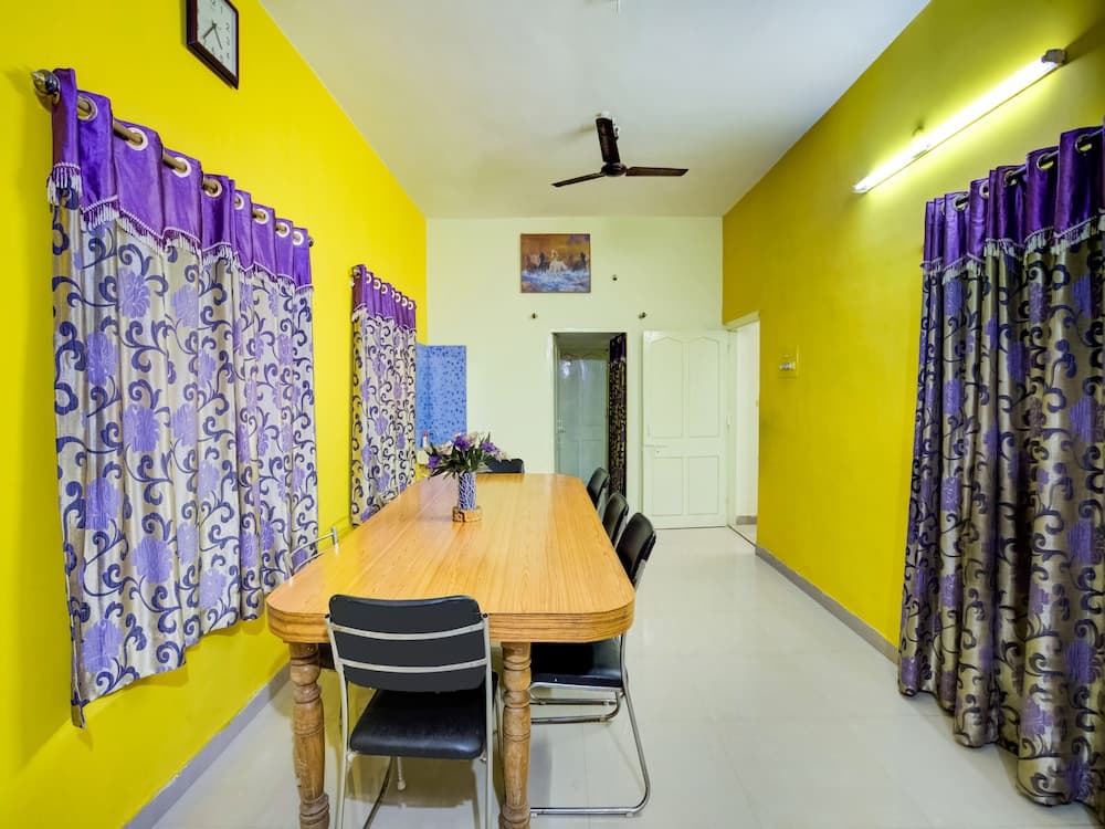 A cozy dining room with vibrant yellow walls, purple patterned curtains, and a wooden table set for gatherings, ideal for travelers seeking a warm and inviting accommodation space.
