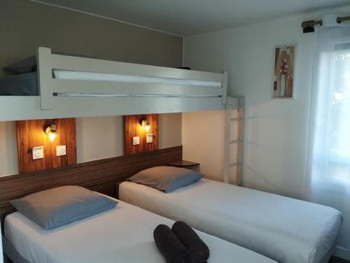A cozy hostel room features bunk beds with neatly made white linens, wooden paneling, soft lighting, and a window with sheer curtains, ideal for budget travelers seeking comfort and simplicity.