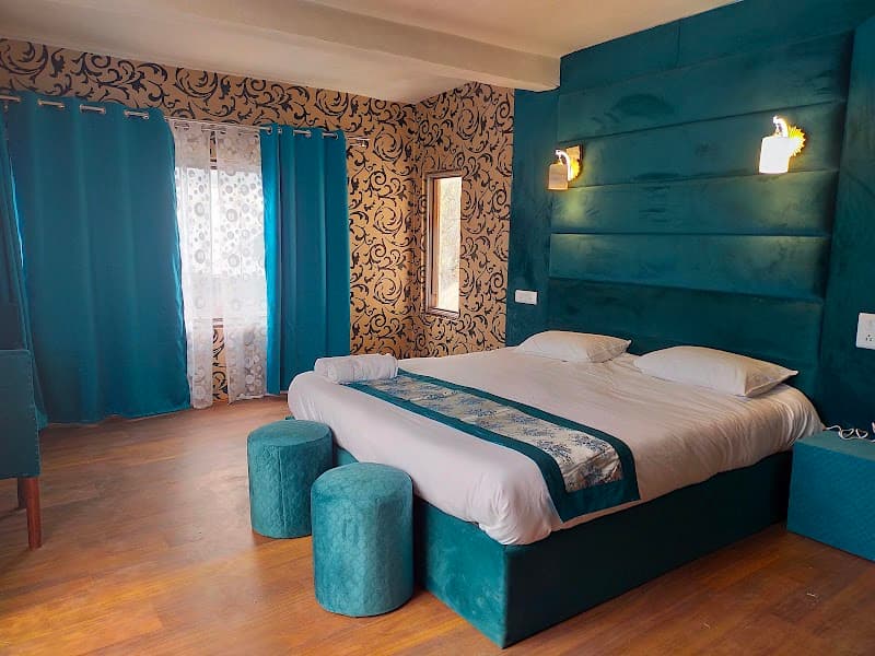 A cozy bedroom at Sarwa Cottage Gulmarg features teal accents, patterned wallpaper, and warm lighting, creating an inviting atmosphere ideal for travelers seeking comfort in a serene mountain retreat.
