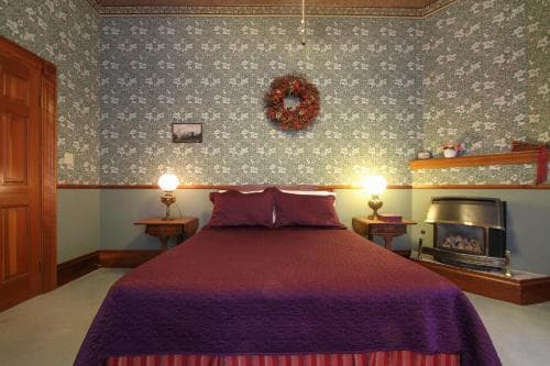 A cozy bedroom with floral wallpaper, a purple bedspread, and a festive wreath exudes warmth and comfort, ideal for a relaxing getaway at a charming inn.