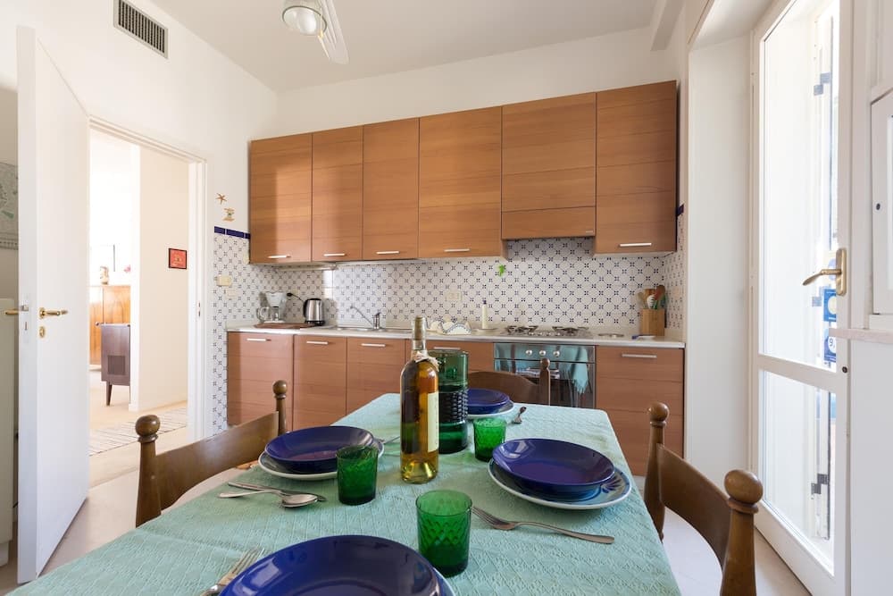 A cozy kitchen-dining area with wooden cabinets, patterned tiles, and a set table featuring blue plates and green glasses, ideal for travelers seeking a homey and inviting rental space.