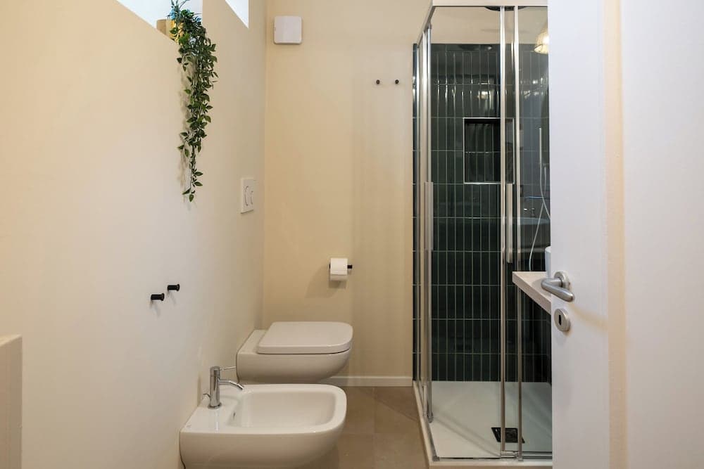 A modern bathroom with a sleek bidet, toilet, and glass-enclosed shower featuring dark tiles exudes a clean and minimalist vibe, ideal for travelers seeking contemporary accommodations.