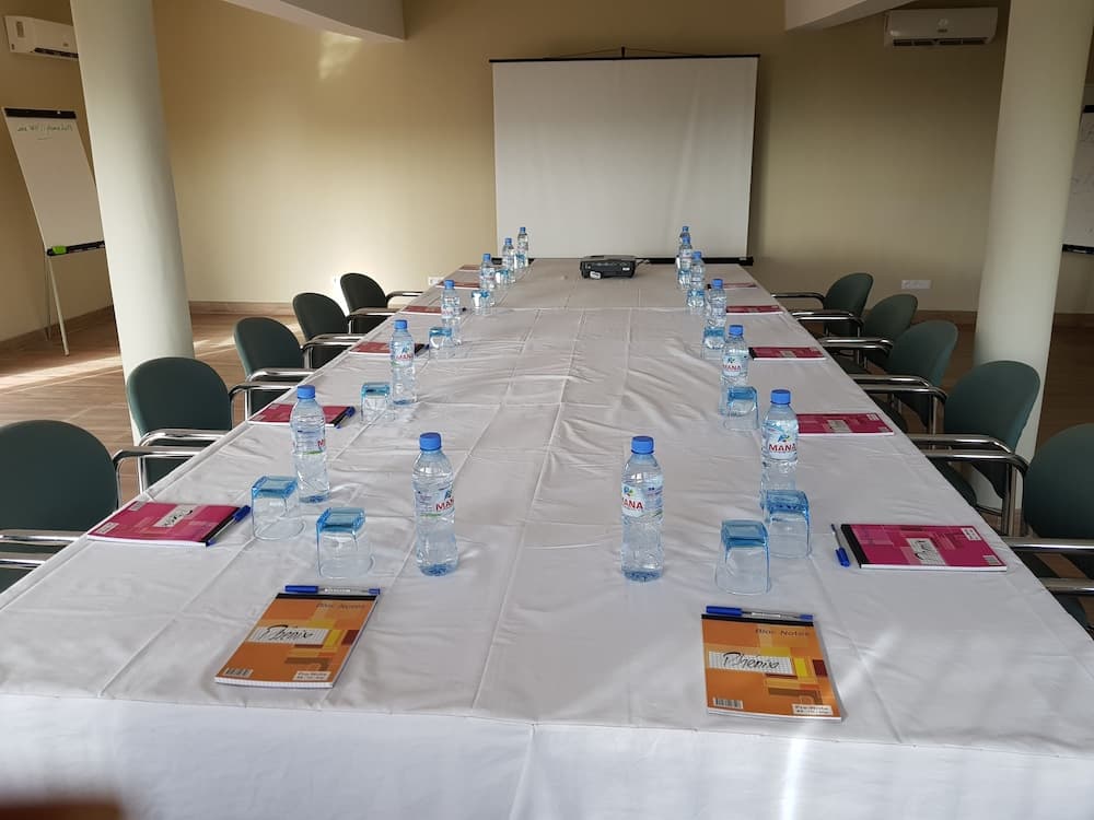 A well-lit conference room set up for a professional meeting features a long table lined with water bottles, notebooks, and pens, ideal for business travelers seeking a productive workspace.