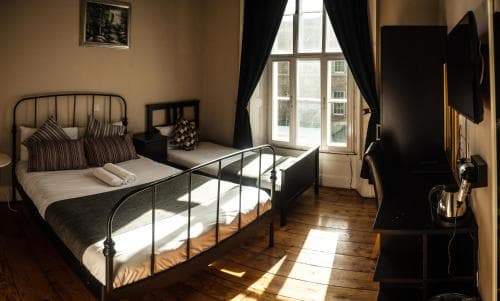 A cozy hotel room with wooden floors, a metal bed frame, and large windows letting in natural light creates a warm and inviting atmosphere, perfect for travelers seeking comfort and relaxation.