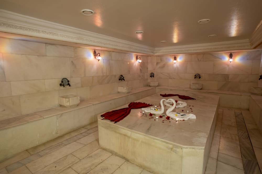A serene Turkish bath features marble walls, soft lighting, and decorative towels shaped like swans, ideal for relaxation and wellness tourism.