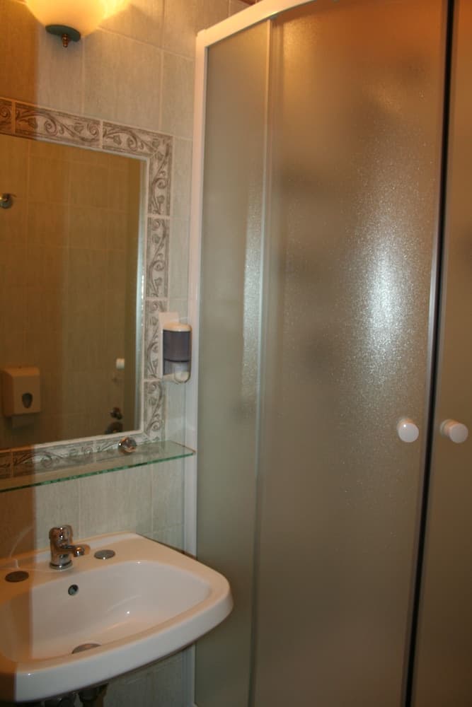 A cozy bathroom features a sleek sink, frosted glass shower doors, and decorative tiled walls, ideal for travelers seeking comfort and cleanliness in their accommodations.