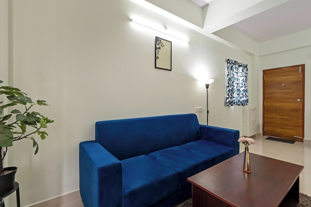 A cozy living room features a vibrant blue sofa, wooden coffee table with flowers, and modern decor, ideal for travelers seeking a comfortable and stylish accommodation.
