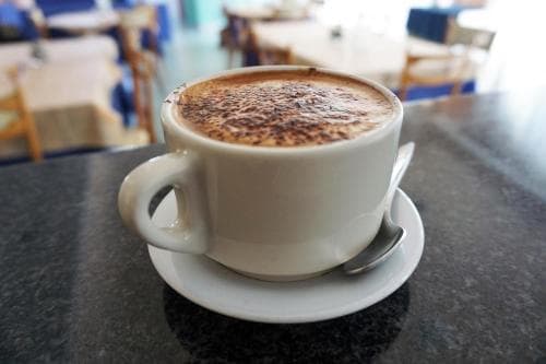 A steaming cup of cappuccino sits invitingly on a café table, surrounded by cozy seating in a relaxed indoor setting, perfect for travelers seeking a quiet moment to unwind.