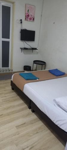 A cozy budget hotel room features a neatly made bed with blue towels, a mounted TV, and simple decor, ideal for travelers seeking affordable accommodation.