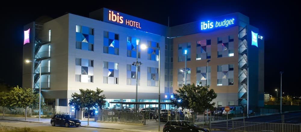 A brightly lit Ibis Hotel and Ibis Budget building at night, featuring modern architecture with geometric windows, creates an inviting atmosphere for travelers seeking accommodation in an urban setting.