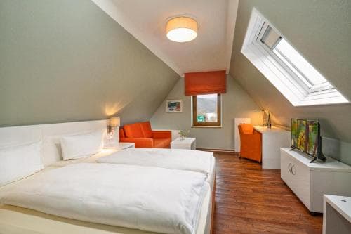 A cozy attic bedroom with sloped ceilings, warm wooden floors, orange accents, and skylights offers a serene retreat for travelers seeking comfort and relaxation.