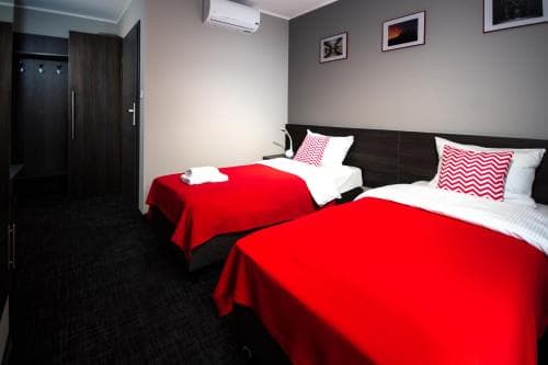 A cozy hotel room features two beds with vibrant red bedding against a modern gray wall, creating a welcoming atmosphere ideal for travelers seeking comfort and style.