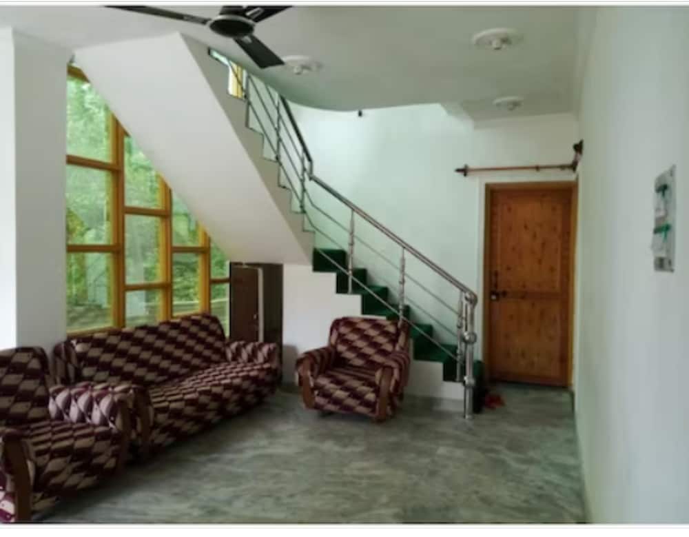 A cozy living room with patterned sofas, a staircase leading to an upper level, and large windows offering a serene view of greenery, ideal for travelers seeking a tranquil accommodation experience.