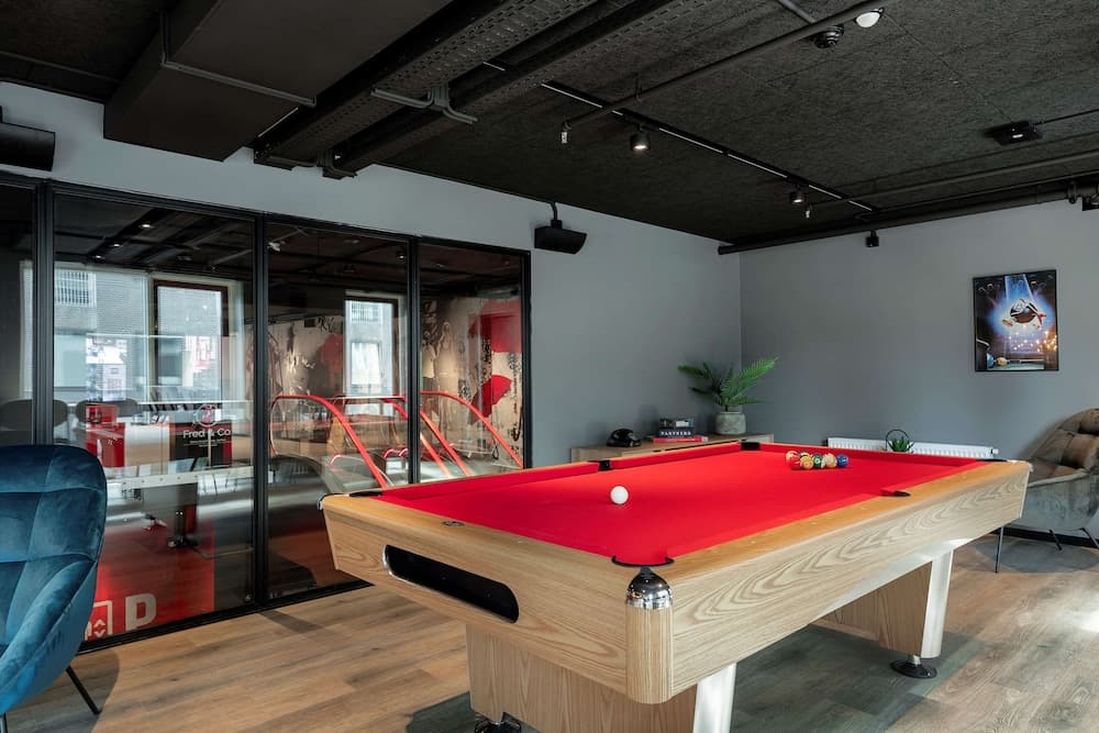 A cozy indoor recreational space features a vibrant red pool table, modern furnishings, and large glass windows, creating an inviting atmosphere ideal for leisure activities and team-building events.