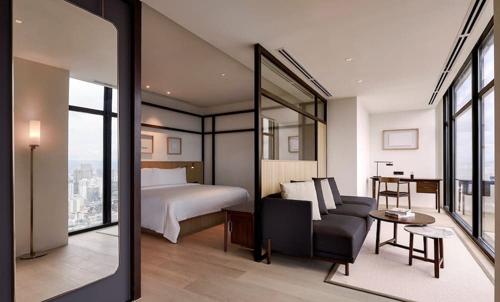 A modern hotel suite with sleek furnishings, large windows offering city views, and a cozy seating area creates an inviting atmosphere ideal for business travelers seeking comfort and style.