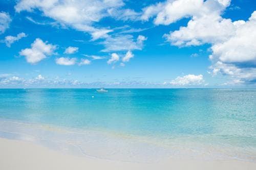 A serene tropical beach scene with pristine white sand, crystal-clear turquoise waters, and a bright blue sky dotted with fluffy clouds, ideal for relaxation and vacation photography.