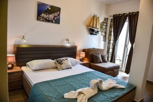 A cozy hotel room with a neatly made bed, nautical-themed decor, and large windows draped in brown curtains, ideal for travelers seeking comfort and a seaside ambiance.