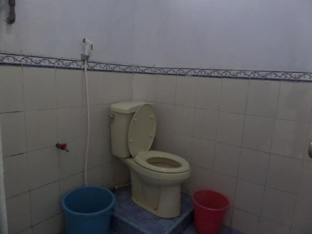 A simple tiled bathroom with a toilet, bidet hose, and colorful buckets offers a functional space for travelers seeking basic amenities in budget accommodations.