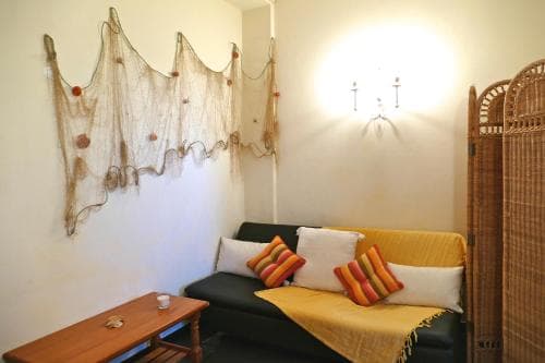 A cozy living room with a black sofa adorned with striped pillows, a wooden coffee table, and a decorative fishing net on the wall, creating a relaxed and artistic atmosphere ideal for a traveler seeking a unique accommodation experience.
