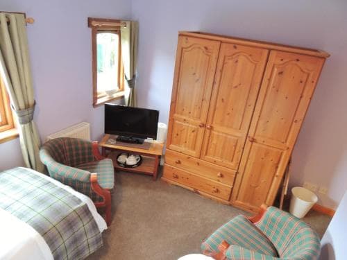 A cozy bedroom with plaid-patterned furniture, a wooden wardrobe, and a small TV by the window, ideal for travelers seeking a comfortable and quaint accommodation experience.