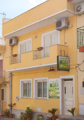 A charming yellow building with white shutters and balconies, featuring a "Gigi" sign, exudes a cozy Mediterranean vibe ideal for travelers seeking a quaint accommodation experience.