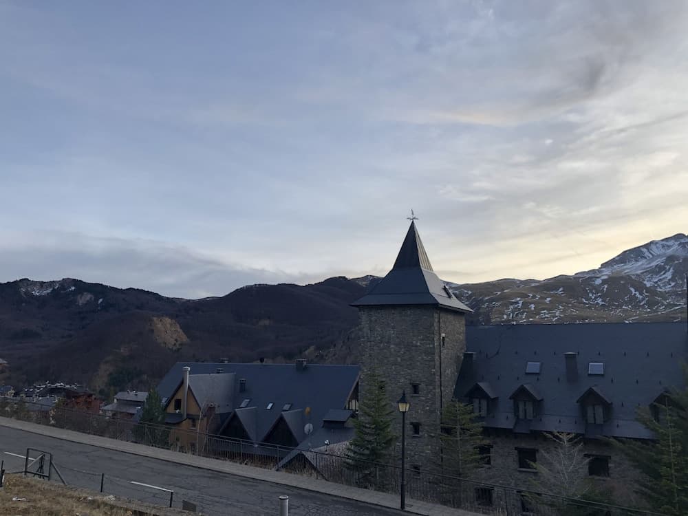 A serene mountain village features a stone church with a pointed spire under a soft twilight sky, ideal for travelers seeking peaceful retreats amidst nature.