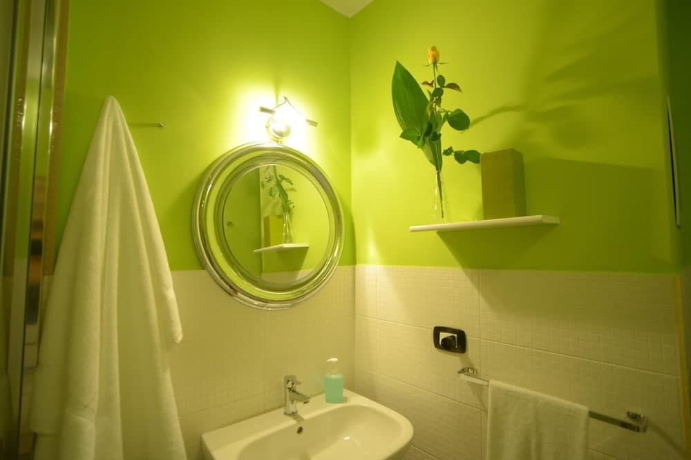 A cozy bathroom with vibrant lime green walls, a round mirror, and a delicate flower on a shelf creates a refreshing and inviting atmosphere ideal for travelers seeking a unique accommodation experience.