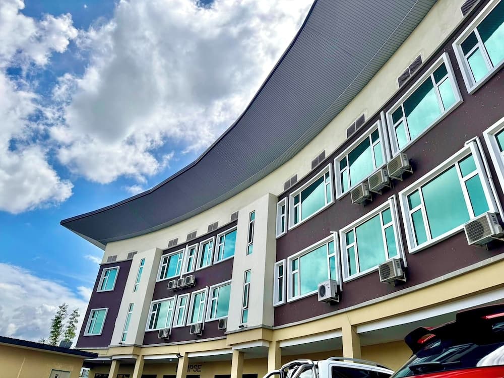 A modern multi-story building with a curved roof and air conditioning units under a partly cloudy sky, ideal for educational or office purposes, captured in a vibrant outdoor setting perfect for business travelers seeking professional environments.