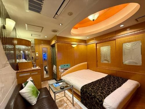 A cozy, warmly lit capsule hotel room features a neatly made bed, wooden paneling, and modern amenities, ideal for travelers seeking comfort in compact urban accommodations.